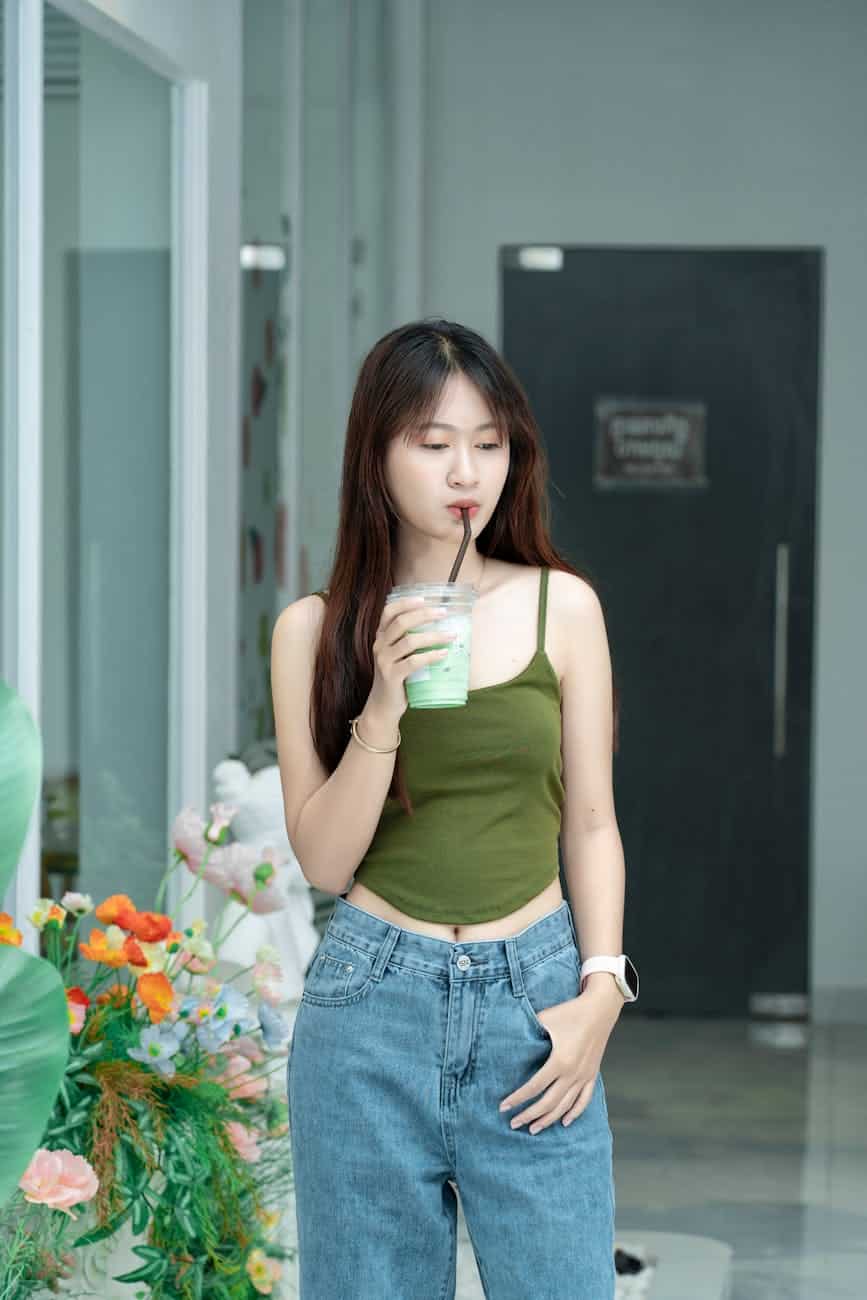 a woman in a green tank top and jeans drinking a drink